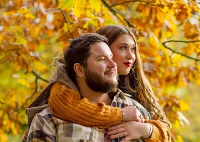 A loving couple captured in a warm embrace during Autumn, with beautiful warm autumnal foliage creating a soft background.